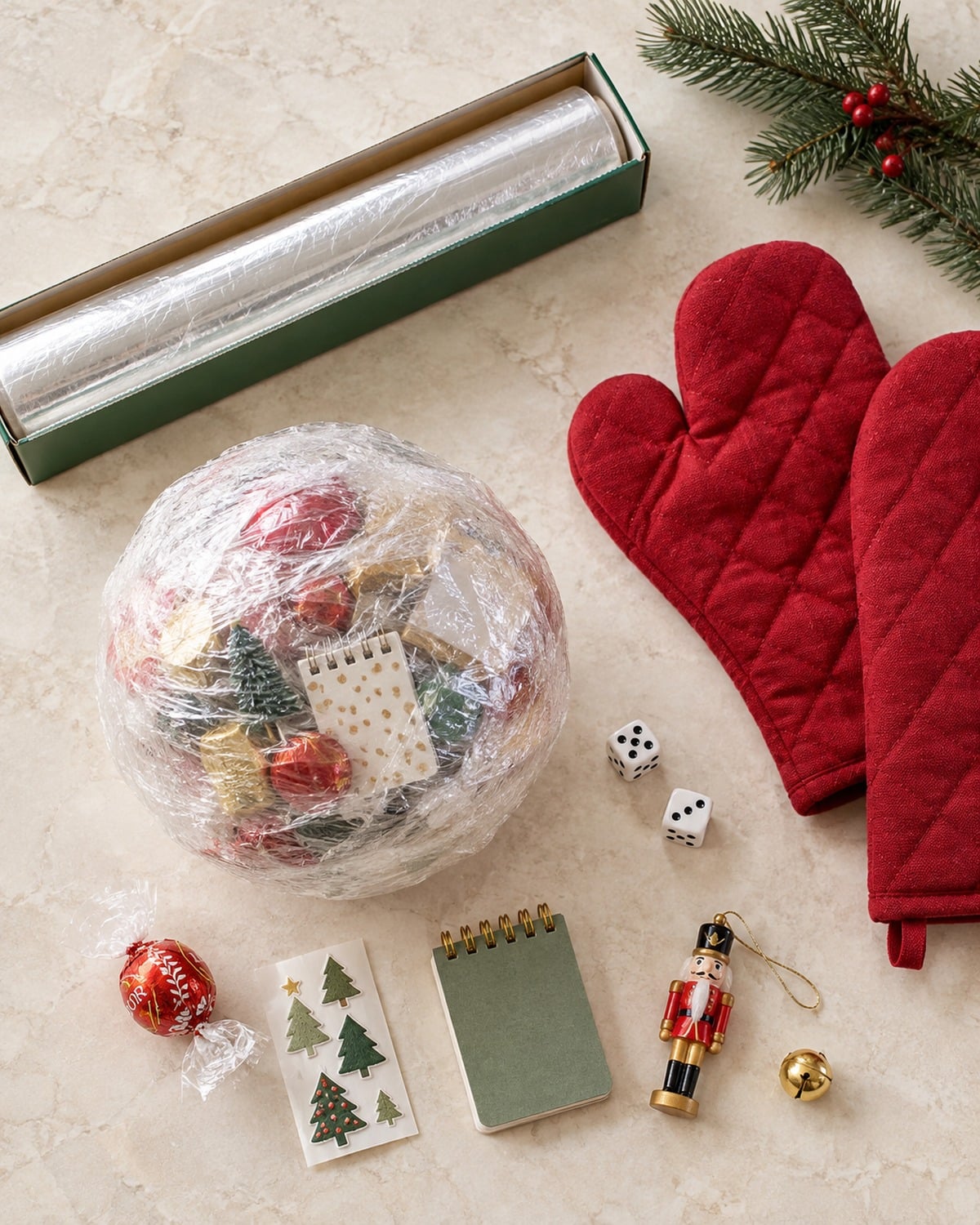 Saran Wrap Ball Game: Rules, Prize Ideas and Christmas Variations 2 Plastic wrap prize ball, roll of plastic wrap, oven mitts, dice, and small Christmas prizes arranged on a light stone surface
